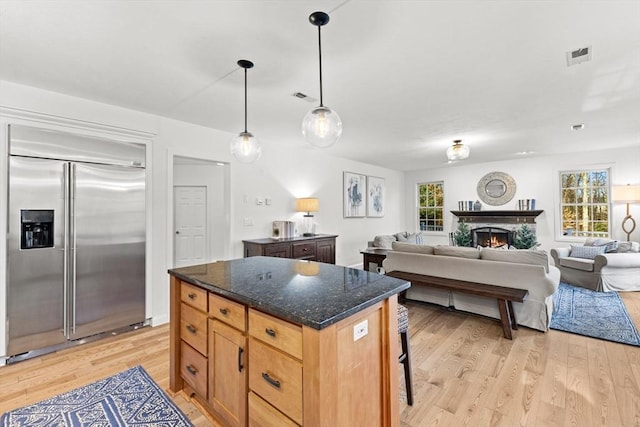 kitchen featuring a breakfast bar area, decorative light fixtures, dark stone countertops, built in fridge, and light hardwood / wood-style floors