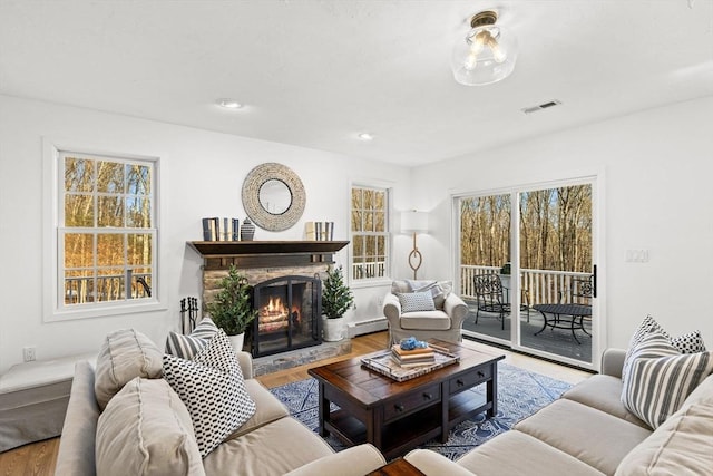 living room with a baseboard radiator, a stone fireplace, and light hardwood / wood-style flooring