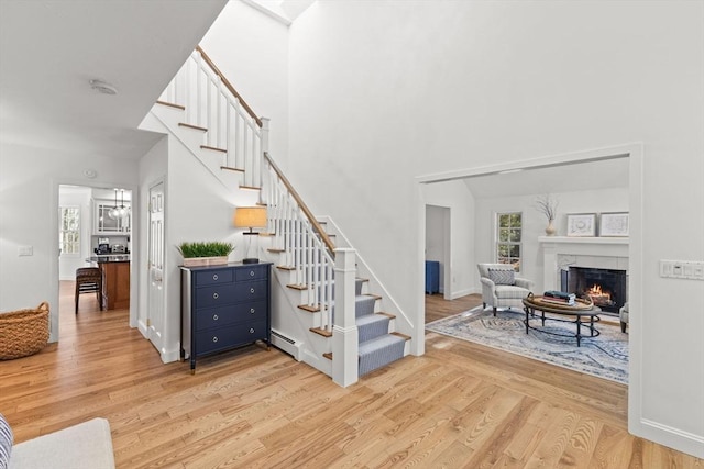 staircase featuring wood-type flooring, a high ceiling, and baseboard heating