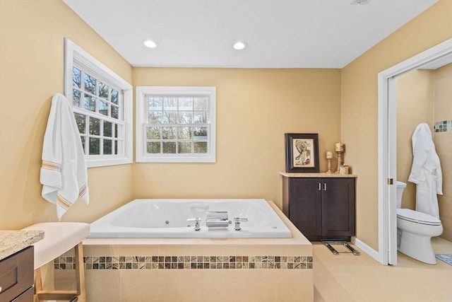 bathroom with vanity, tiled tub, and toilet