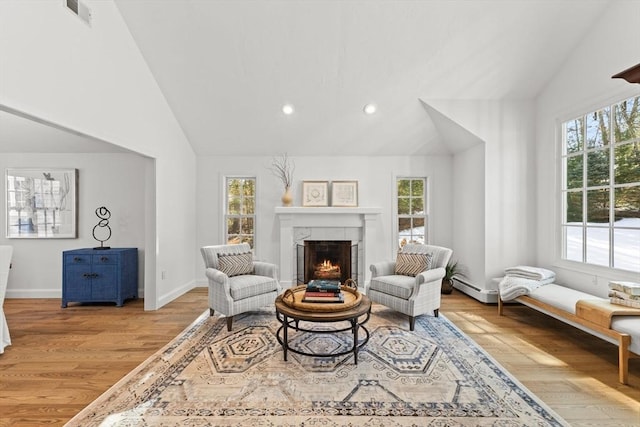 living area with a tile fireplace, a baseboard heating unit, a wealth of natural light, and light hardwood / wood-style floors