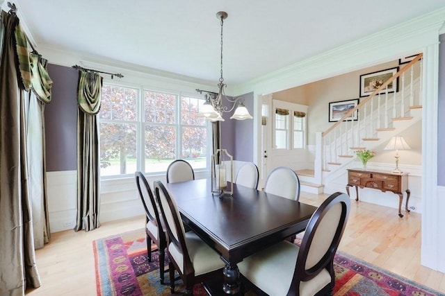 dining area with a chandelier, stairway, wood finished floors, a wainscoted wall, and healthy amount of natural light