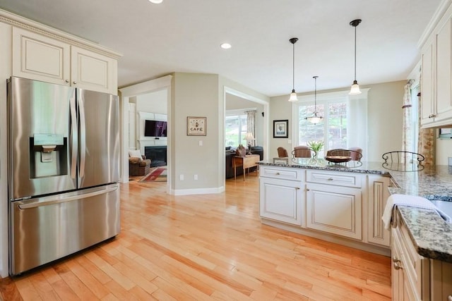 kitchen featuring stainless steel refrigerator with ice dispenser, a peninsula, light wood-type flooring, a fireplace, and light stone counters