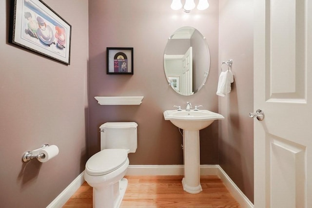 half bathroom with toilet, wood finished floors, and baseboards
