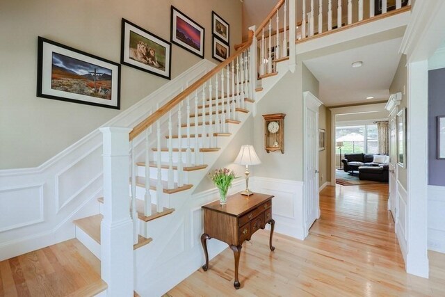 stairs with a decorative wall, wood finished floors, and a wainscoted wall