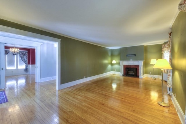 unfurnished living room featuring ornamental molding, a fireplace, baseboards, light wood-style flooring, and a notable chandelier