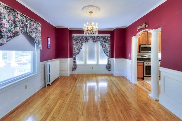 unfurnished dining area featuring an inviting chandelier, a healthy amount of sunlight, radiator heating unit, and a wainscoted wall