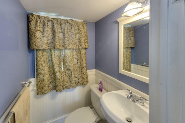 half bathroom featuring a sink, a decorative wall, wainscoting, and toilet