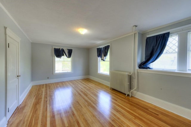 empty room featuring baseboards, a healthy amount of sunlight, radiator, and light wood-type flooring