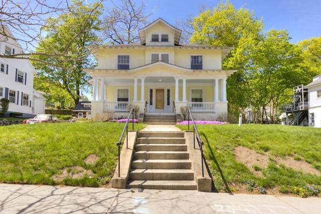 american foursquare style home featuring covered porch, stairway, a front lawn, and stucco siding