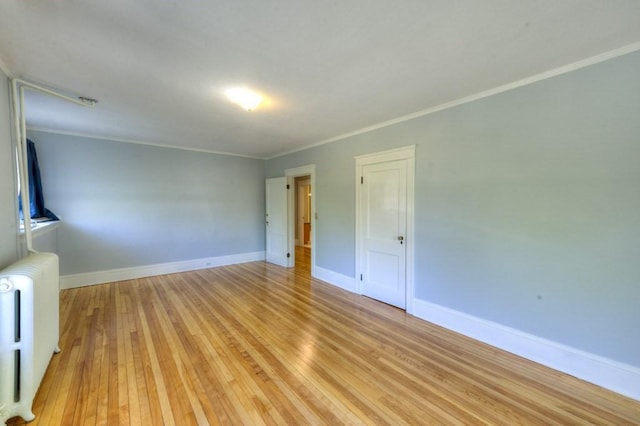empty room with crown molding, baseboards, radiator heating unit, and light wood-style floors