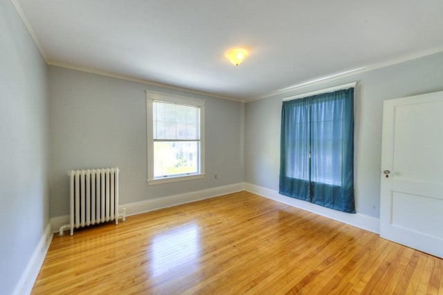 spare room featuring radiator, ornamental molding, baseboards, and light wood finished floors