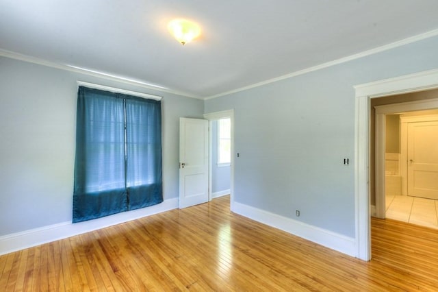 spare room featuring crown molding, baseboards, and light wood-type flooring