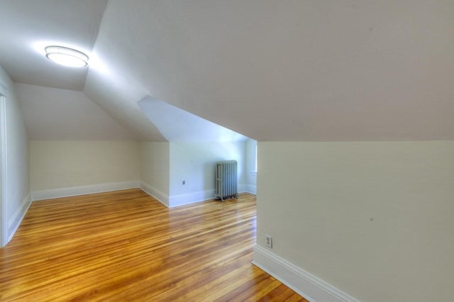 additional living space with baseboards, vaulted ceiling, radiator heating unit, and light wood-style flooring