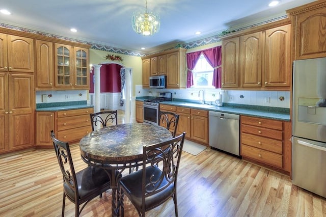 kitchen featuring brown cabinetry, dark countertops, a sink, glass insert cabinets, and stainless steel appliances