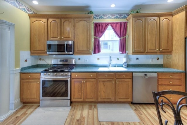 kitchen with brown cabinetry, a sink, light wood-style flooring, appliances with stainless steel finishes, and backsplash