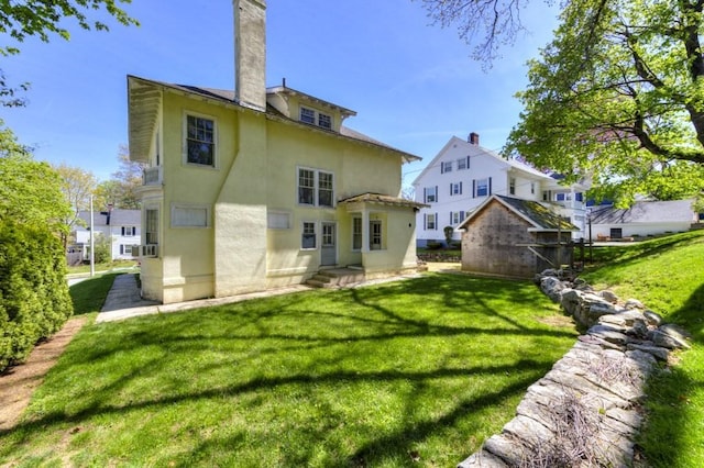 rear view of house with a lawn, an outdoor structure, stucco siding, and a chimney