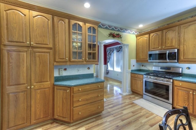kitchen featuring decorative columns, dark countertops, glass insert cabinets, arched walkways, and stainless steel appliances