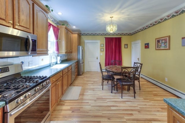 kitchen featuring appliances with stainless steel finishes, baseboard heating, brown cabinets, a sink, and a notable chandelier