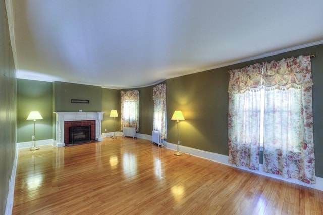 unfurnished living room with crown molding, wood finished floors, radiator, and a fireplace