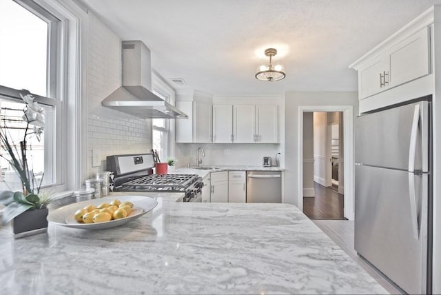 kitchen featuring sink, appliances with stainless steel finishes, plenty of natural light, wall chimney range hood, and white cabinets