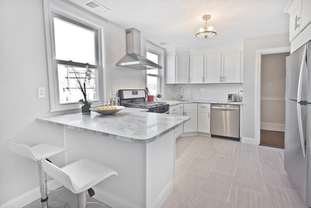 kitchen featuring wall chimney exhaust hood, a breakfast bar area, white cabinetry, appliances with stainless steel finishes, and kitchen peninsula