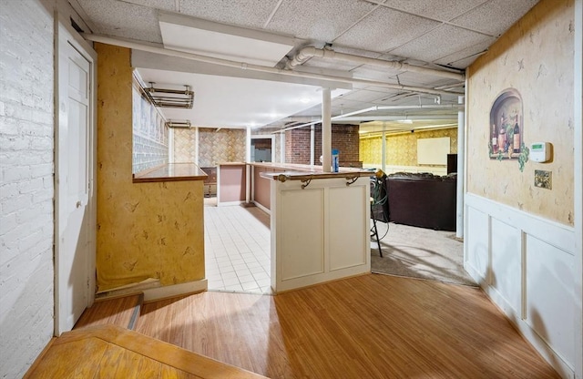 116 Adin St, Hopedale, MA 01747 - kitchen featuring light wood-style floors, open floor plan, a wainscoted wall, brick wall, and a paneled ceiling
