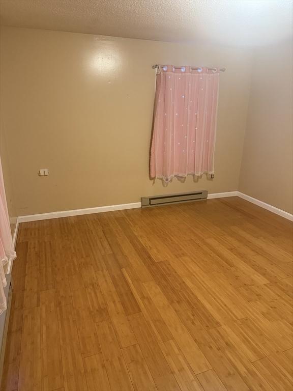 empty room with a textured ceiling, baseboard heating, light wood-style flooring, and baseboards