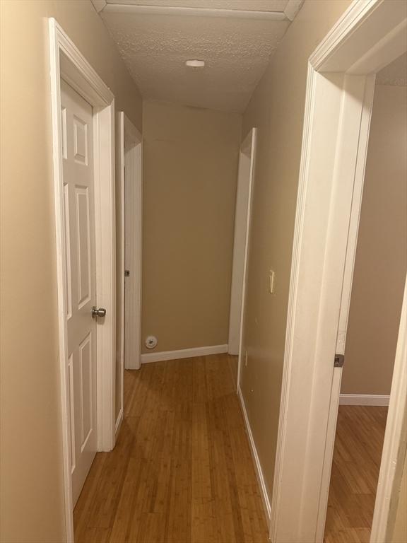 corridor featuring light wood finished floors, baseboards, and a textured ceiling