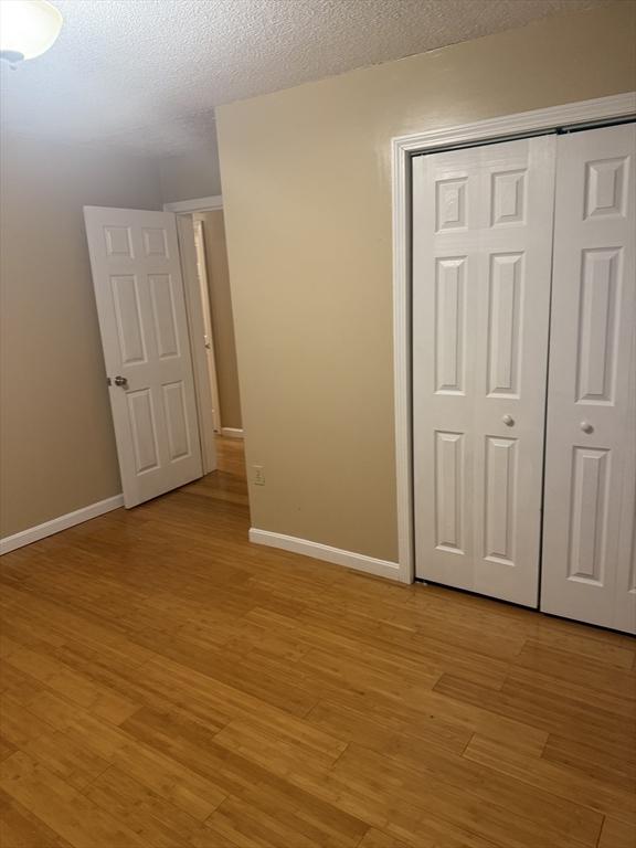 unfurnished bedroom featuring a closet, baseboards, a textured ceiling, and light wood finished floors