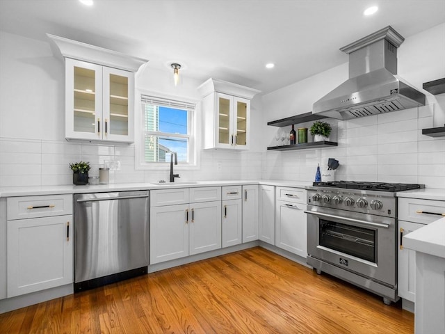 kitchen with appliances with stainless steel finishes, white cabinets, island exhaust hood, light hardwood / wood-style floors, and sink