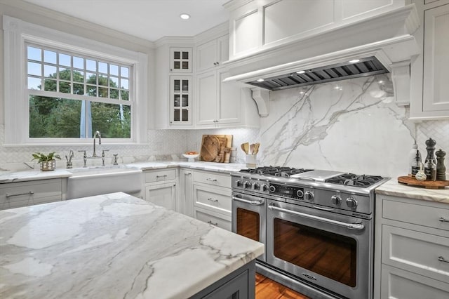 kitchen featuring a sink, premium range hood, tasteful backsplash, white cabinets, and double oven range