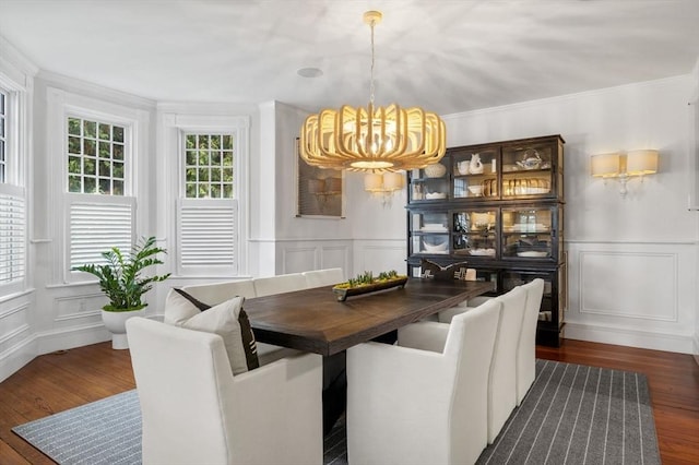 dining area featuring wainscoting, a decorative wall, crown molding, a chandelier, and dark wood-style floors