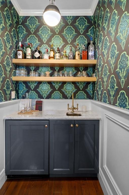 bar with indoor wet bar, a sink, wallpapered walls, crown molding, and dark wood-style floors