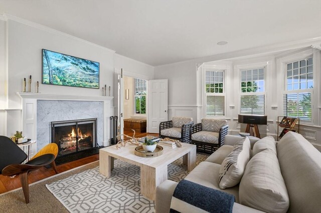living room featuring a decorative wall, a wainscoted wall, a high end fireplace, wood finished floors, and crown molding