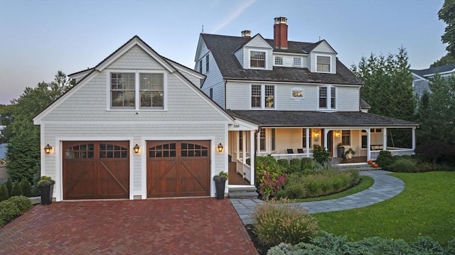 view of front of property with an attached garage, a chimney, decorative driveway, a front yard, and a porch
