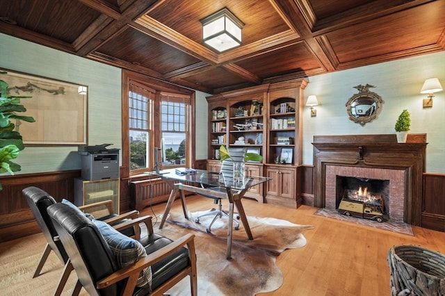 office space featuring light wood-style flooring, coffered ceiling, a wainscoted wall, a brick fireplace, and wooden ceiling