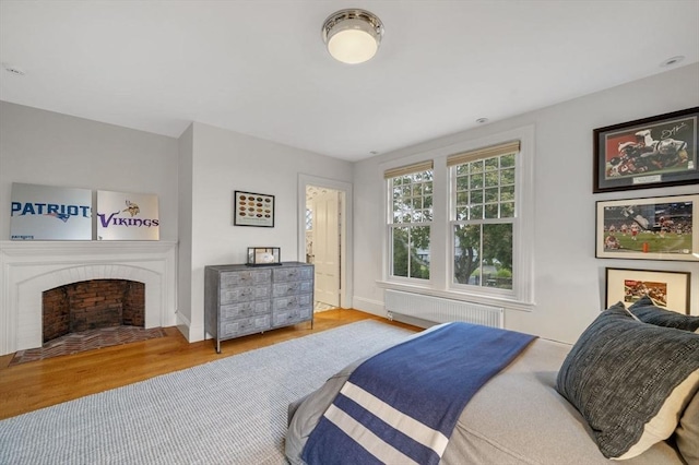 bedroom with baseboards, radiator, a brick fireplace, and wood finished floors