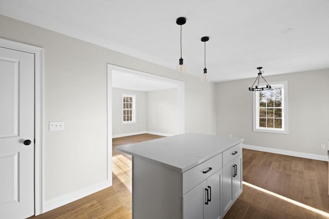 kitchen with a center island, gray cabinets, decorative light fixtures, light stone counters, and wood-type flooring