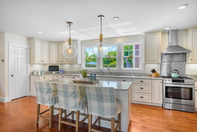 27 Watcha Path, Edgartown, MA 02539 - kitchen featuring stainless steel gas range, wall chimney range hood, light wood-style floors, light stone countertops, and a breakfast bar