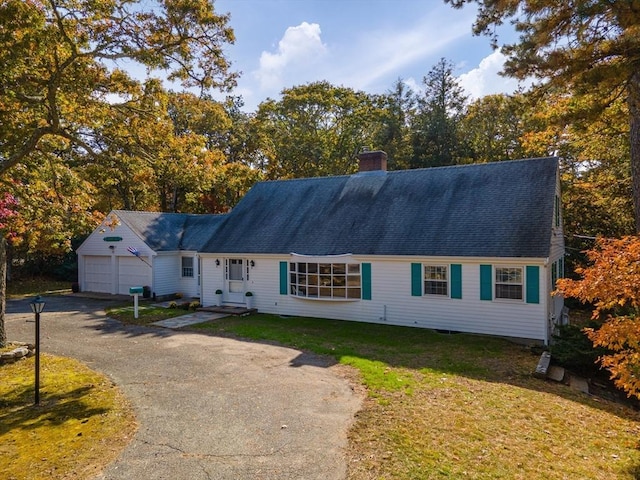 view of front of house featuring driveway, an attached garage, a chimney, and a front lawn