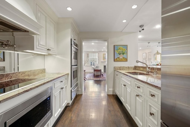 kitchen featuring dark wood-type flooring, custom range hood, stainless steel appliances, white cabinetry, and a sink