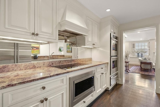 kitchen with light stone countertops, custom range hood, stainless steel appliances, white cabinetry, and dark wood-style flooring