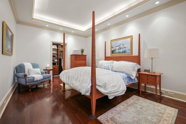 bedroom with wood finished floors, baseboards, a tray ceiling, a spacious closet, and crown molding