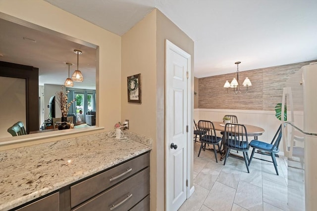 547 Washington St Unit B13, Pembroke, MA 02359 - kitchen with freestanding refrigerator, a chandelier, a wainscoted wall, decorative light fixtures, and light stone countertops