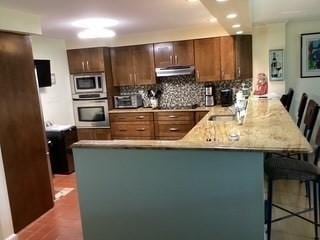 154 Lynnway Unit 309, Lynn, MA 01902 - kitchen with stainless steel appliances, a peninsula, under cabinet range hood, a breakfast bar area, and backsplash