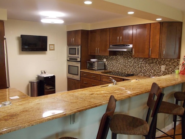 154 Lynnway Unit 309, Lynn, MA 01902 - kitchen with appliances with stainless steel finishes, under cabinet range hood, decorative backsplash, a breakfast bar area, and recessed lighting