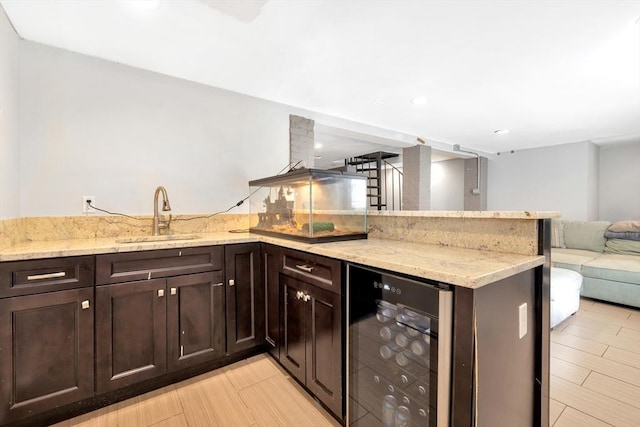 kitchen featuring sink, wine cooler, kitchen peninsula, light stone countertops, and dark brown cabinets