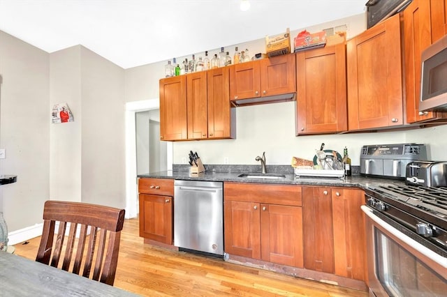 kitchen with sink, stainless steel appliances, light hardwood / wood-style floors, and dark stone counters