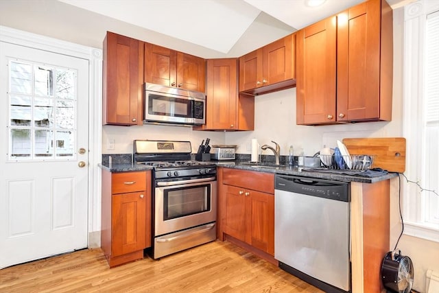 kitchen featuring vaulted ceiling, appliances with stainless steel finishes, sink, dark stone counters, and light wood-type flooring